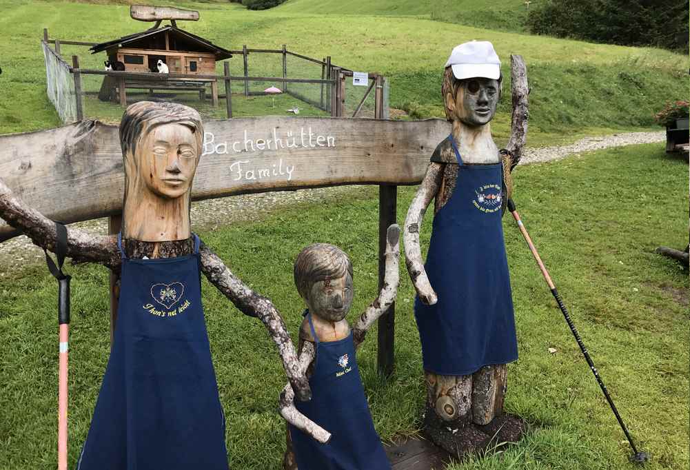 Vor der Bacherhütte steht die Familie aus Holz und begrüßt die Wanderer