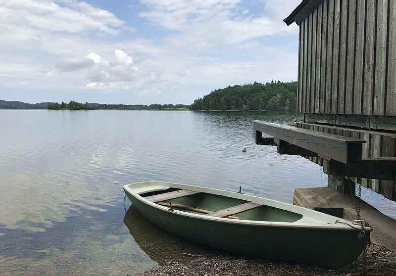 Staffelsee Radweg: Direkt am Ufer des Staffelsees fahren wir mit dem Fahrrad entlang. Unterwegs gibt es Hütten und auch Ruderboote zu sehen.