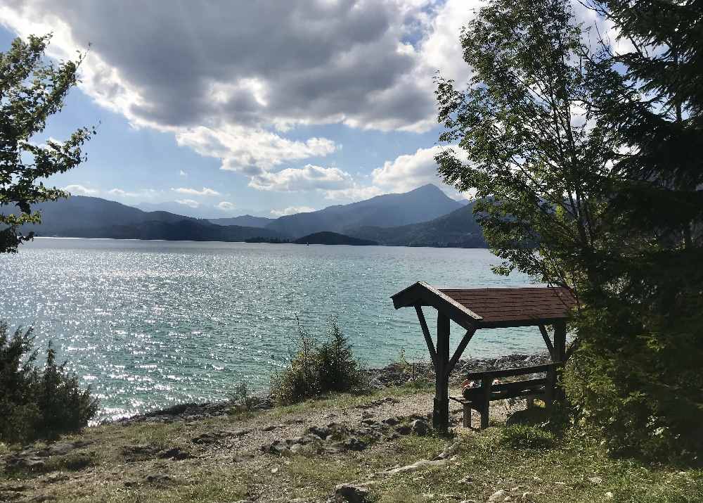 Walchensee Radweg: Oberhalb der Felsen sitzen wir auf der Aussichtsbank und schauen über das Wasser und auf die Berge 