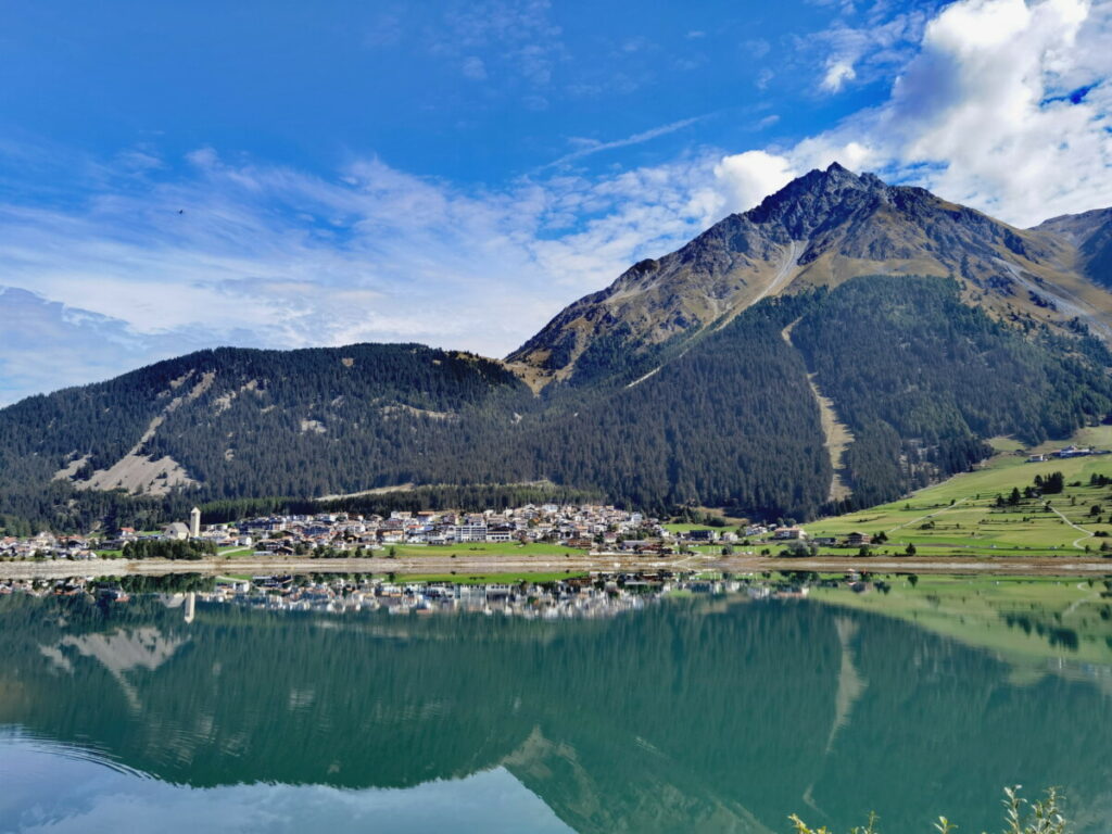 Blick über den Reschensee auf den Ort Reschen und die Berge