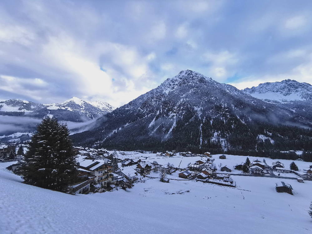 Links im Bild das Hotel Rosenhof Kleinwalsertal, dahinter die Winterlandschaft mit den Bergen