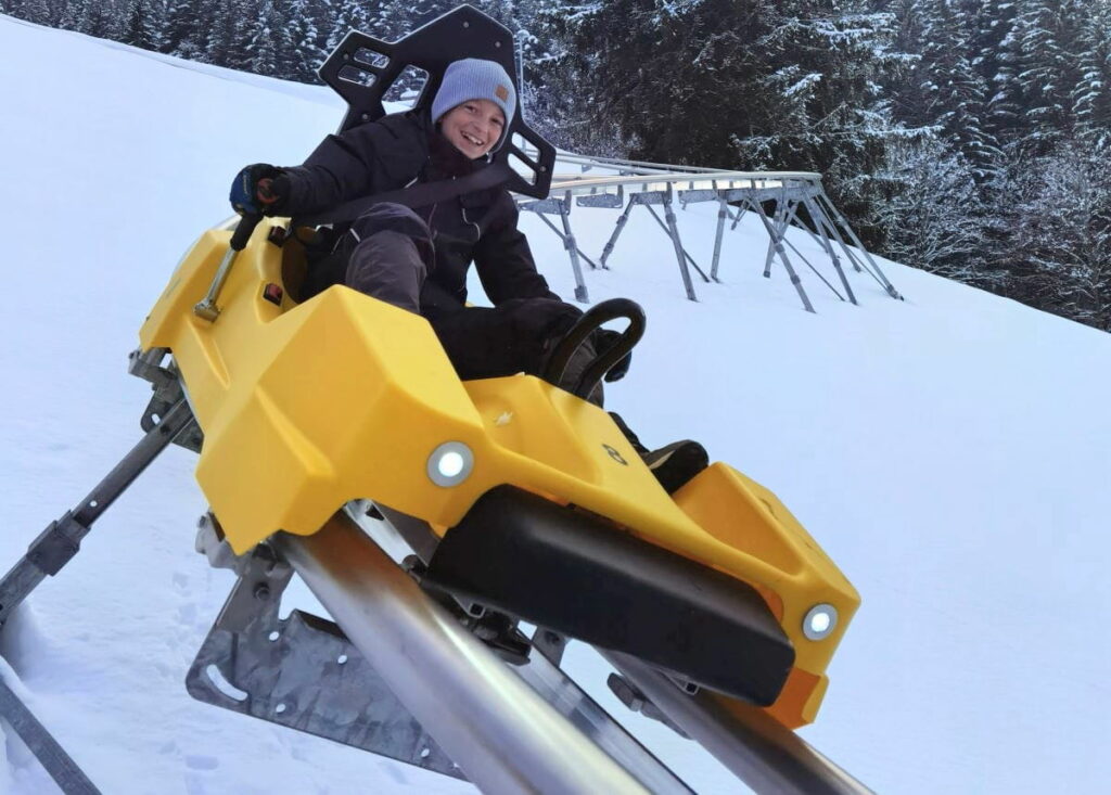 Winterurlaub mit Kindern ohne Ski - der gelbe Coaster bietet für die Kinder sehr viel Spaß! Willst du das Gefährt auch mal lenken?
